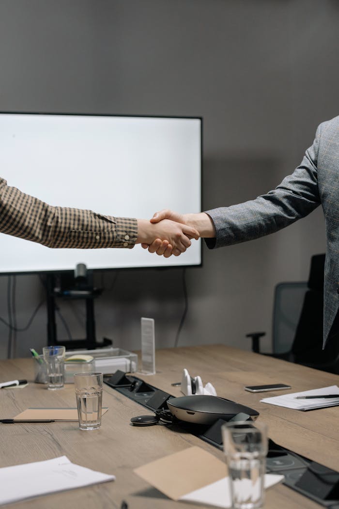 Home Two business professionals shaking hands in a modern meeting room, symbolizing successful collaboration.